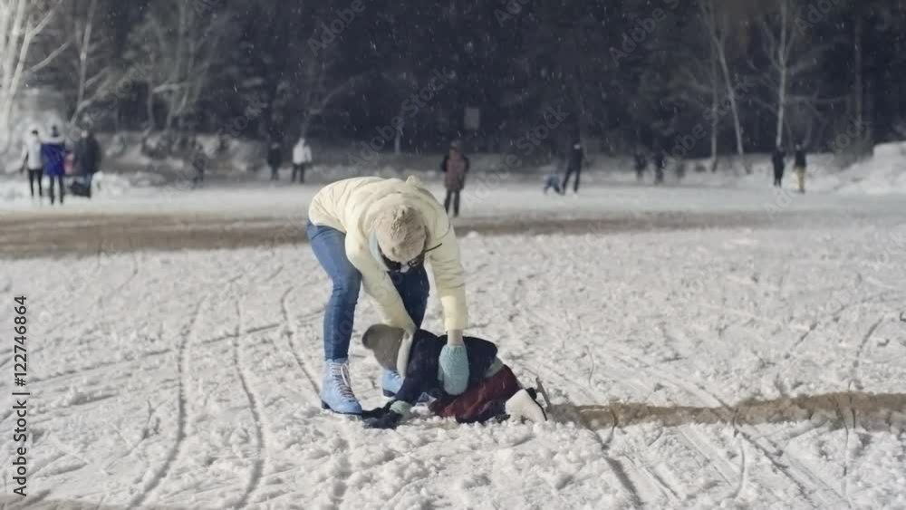 Dolly shot of young woman holding little girl and helping her to skate on ice rink on snowy winter evening Dolly shot of young woman holding little girl and helping her to skate on ice rink on snowy winter evening