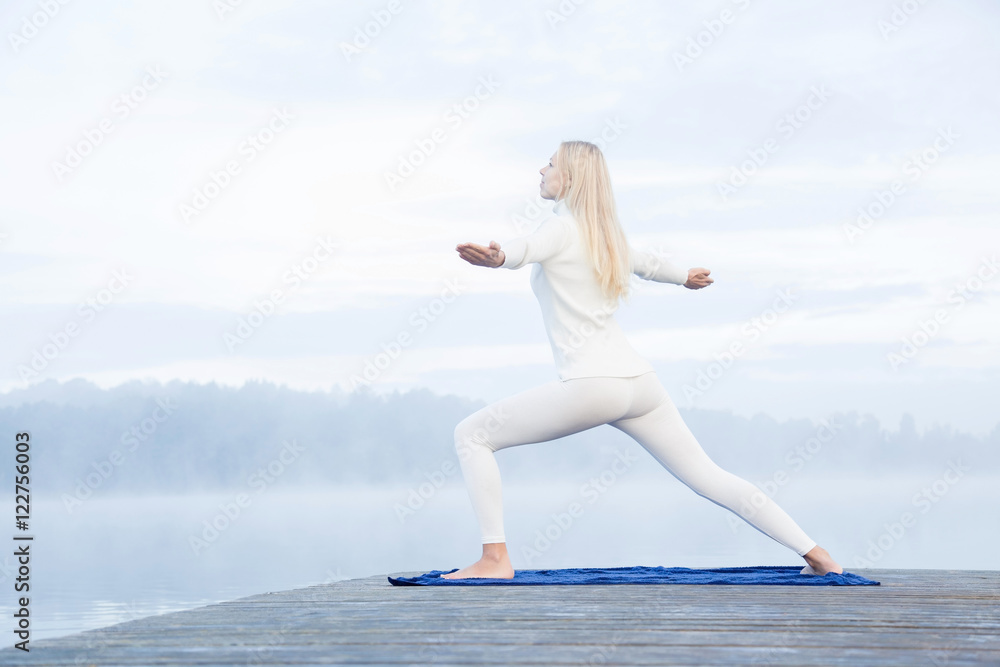 Young woman gymnastics in the mist on the lake footbridge early morning. Peaceful atmosphere. Foggy air.