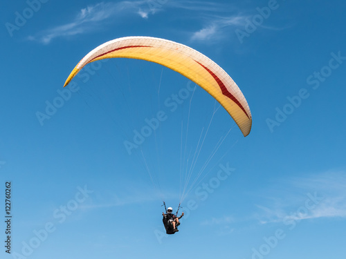 Paraglider flying in blue sky.