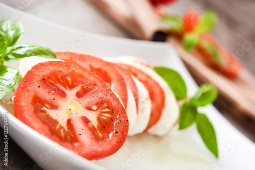Caprese salad with mozzarella cheese, tomatoes and basil on rustic wooden table