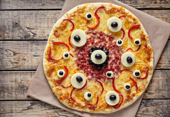 Halloween creative scary food monster pizza snack with eyes on vintage wooden table background. Traditional homemade celebration party decoration