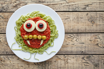 Green spaghetti pasta creative spooky halloween vegetarian food vampire monster with smile, fake blood tomato sauce and funny big mozzarella eyeballs holiday decoration kid party meal on vintage table
