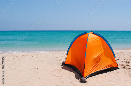 Una tenda arancione su una spiaggia bianca con acqua cristallina