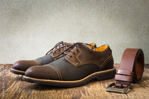 Men's accessories with brown shoes and belt on wooden table over grunge background, still life style