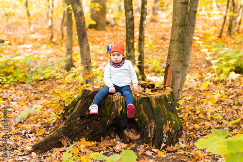 Baby girl sitting on the stump in autumn park outdoor