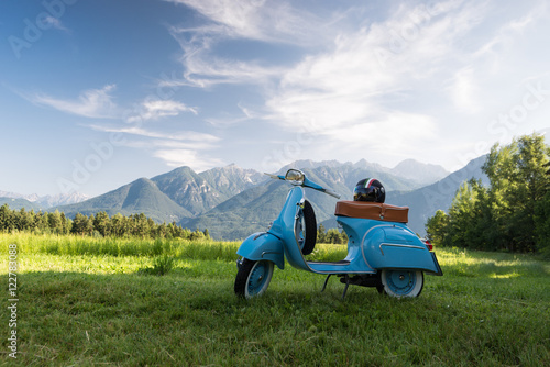Fototapeta Naklejka Na Ścianę i Meble -  Blaue scooter vor Bergkulisse auf Feld