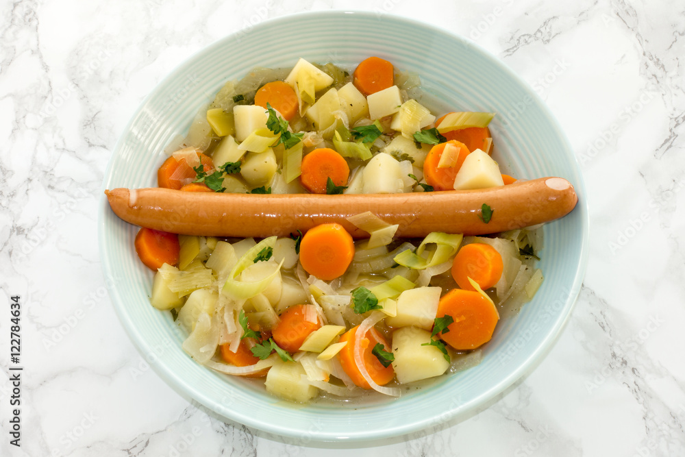 Close-up of a homemade Frankfurter Sausage Stew in a blue soup bowl isolated on white marbled background. 