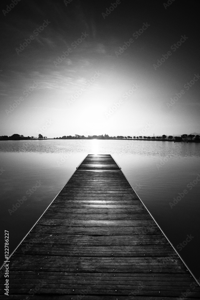 Obraz premium Fotografia czarno-biała, molo o wschodzie słońca w parku Manresa, Katalonia, Hiszpania. Ładny teren spacerowy z drzewami i stawem wodnym