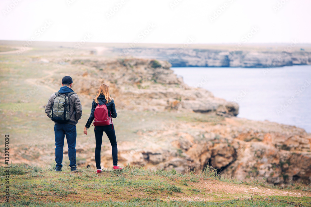 Traveler couple with backpacks standing on the rocky shore in autumn.