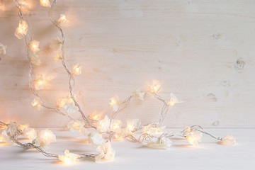 Christmas fairy lights glowing on white wooden background. Cozy festive Xmas garland with warm soft glow on rustic wood wall for holiday greeting card.
