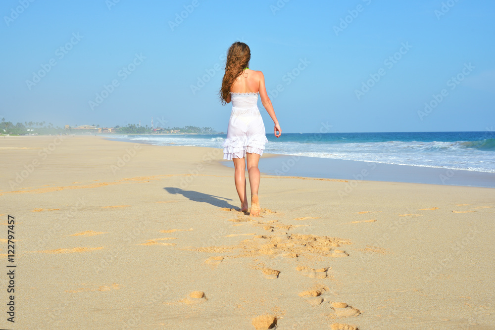 Happy carefree woman walking on beach celebrating her freedom. Summer woman background of the ocean and sand. Back view of girl.