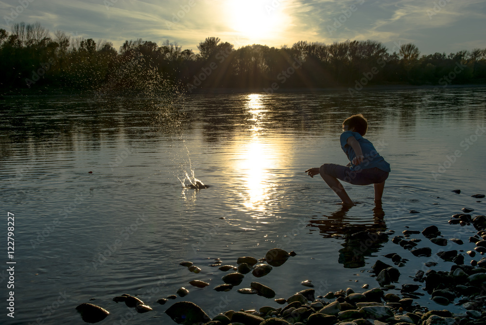Bub wirft Steine in Fluss bei Sonnenuntergang