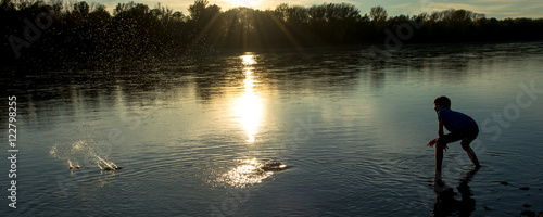 Bub wirft Steine in Fluss bei Sonnenuntergang photo