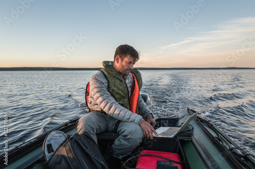 Man is seating in the boat and working with laptop