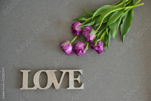 Fresh spring purple tulips flowers bouquet on grey canvas background, word love with wooden texture. Place for text. Green tulips petals, tulips and wood.