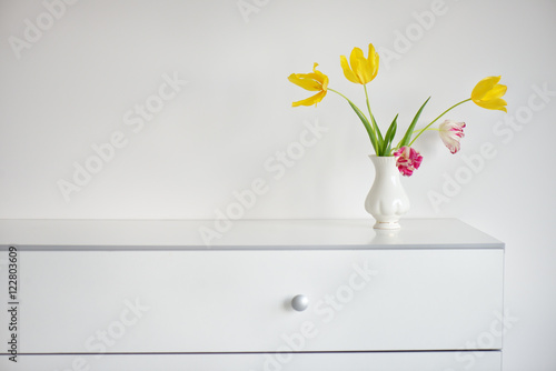 Fotografi interior design scene with a white modern commode and a vase of yellow and pink