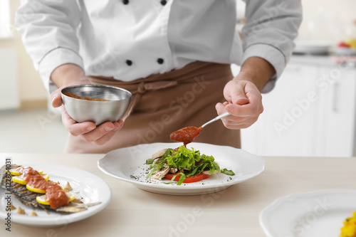 Young chef cook putting tomato sauce on dishes