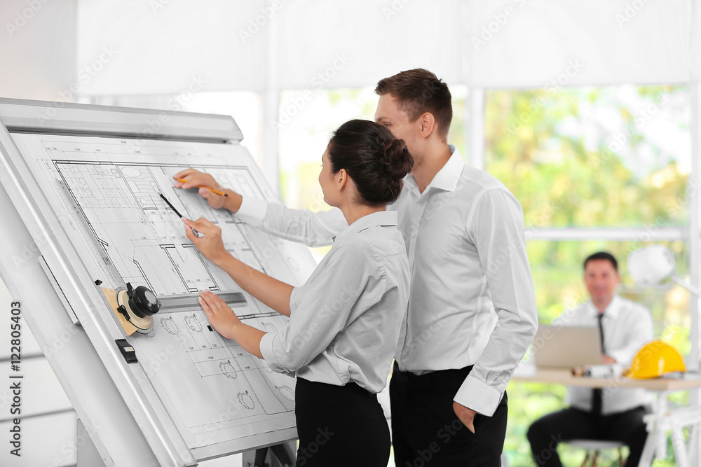 Two young creative engineers working with project on drawing board Two young creative engineers working with project on drawing board