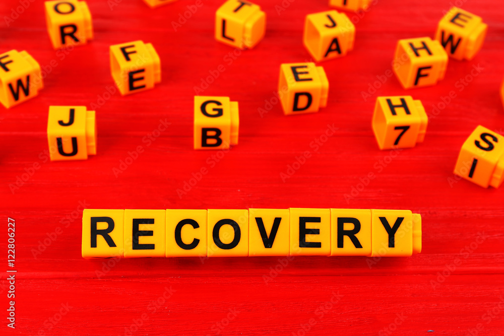 Word recovery made with yellow plastic blocks on wooden background