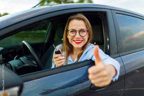 Young happy woman sitting in a car with thumb up