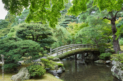 Foto Kyoto, Japan - September 14, 2016: Part of the Japanese garden at the imperial palace showing bow bridge, pond, and multiple trees
