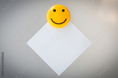 Yellow magnet paper clip on paper note on gray refrigerator background