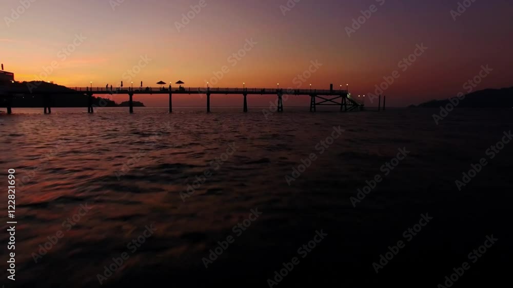 Shooting with drone at sunset in a bay. The drone passes under a pier. Shooting with drone at sunset in a bay. The drone passes under a pier.