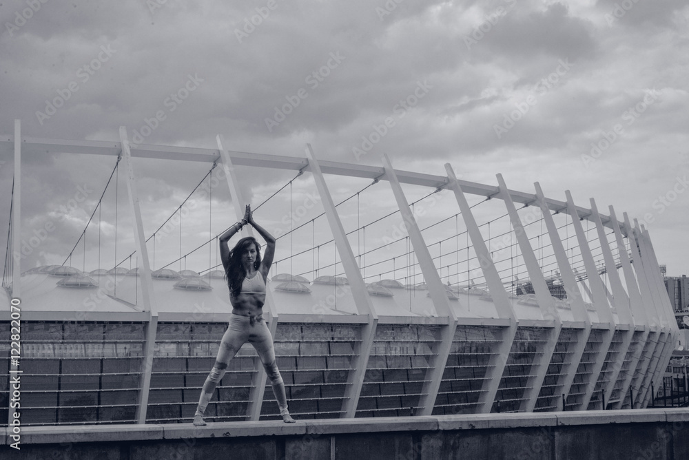 Naklejka premium Woman doing yoga exercises outdoors in the city.Beautiful brunette fit young woman wearing sportswear practicing yoga urban style.Asana, working out,fitness,sport,training and lifestyle concept