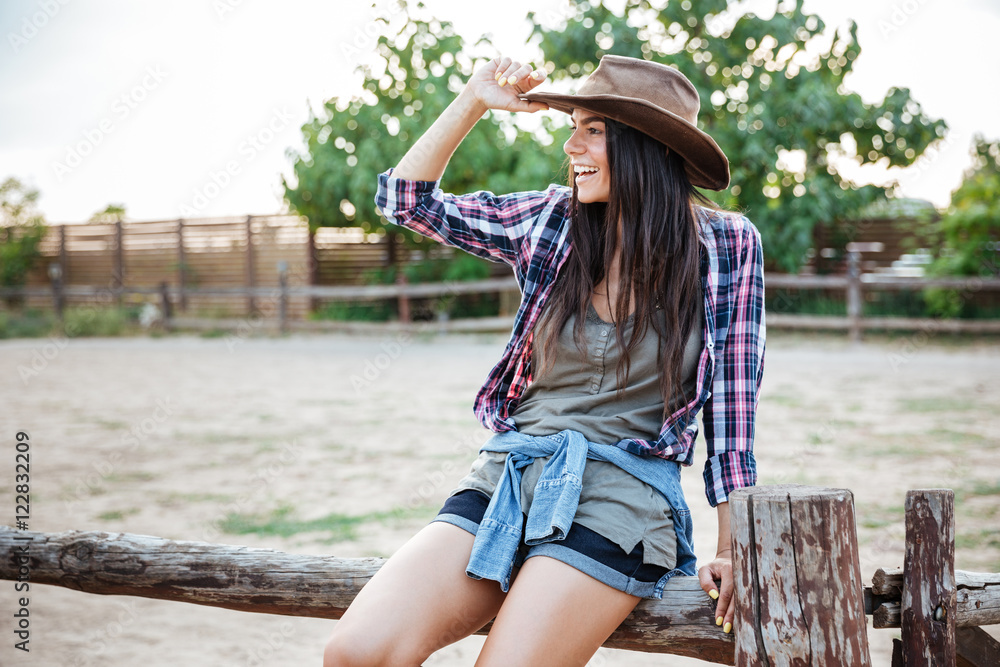 Φωτογραφία Cheerful relaxed young woman cowgirl sitting on fence and smiling