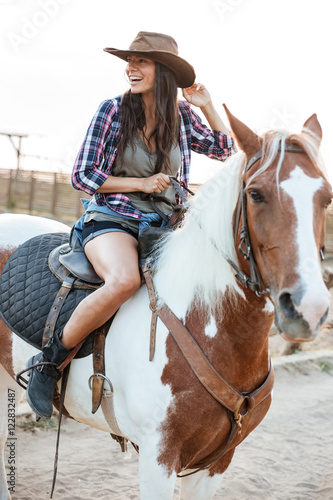 Cheerful woman cowgirl sitting and riding horse in village © Drobot Dean