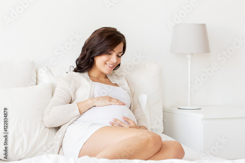 happy pregnant woman lying on bed at home