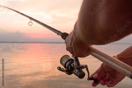 Fisher's hands holding reel, fishing at the sunset