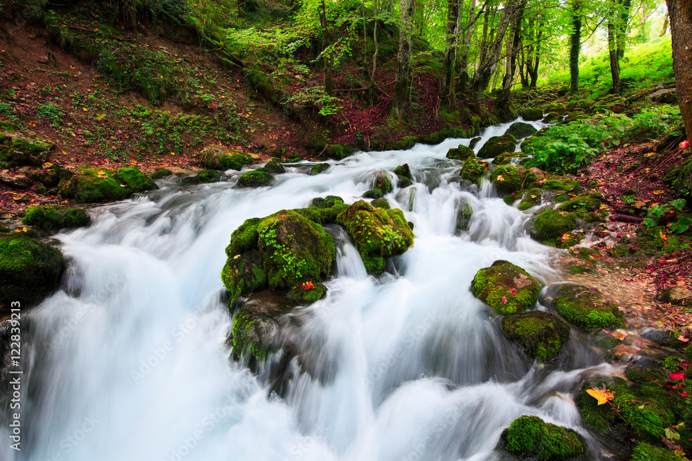 Autumn landscape with mountain river flowing among mossy stones through the colorful forest. Silky smooth stream of clear water. Red leaves frame this beautiful cascade small waterfalls in the wood. Autumn landscape with mountain river flowing among mossy stones through the colorful forest. Silky smooth stream of clear water. Red leaves frame this beautiful cascade small waterfalls in the wood.