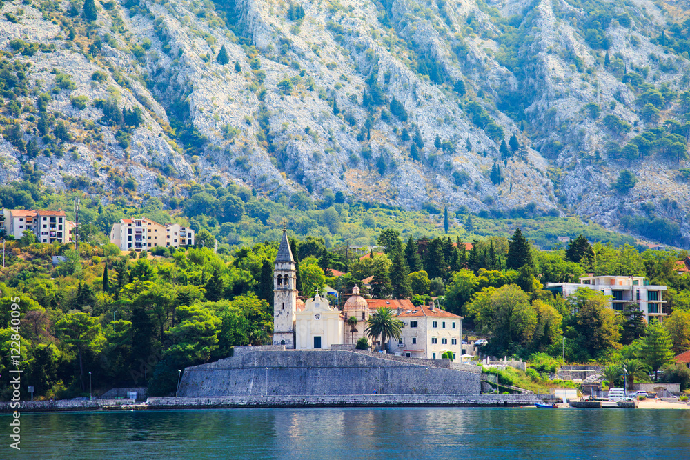 Waterfront of small town Dobrota along Bay of Kotor, Montenegro. View of Church of St Mathew, coastal villas, gardens and mountains from sea.