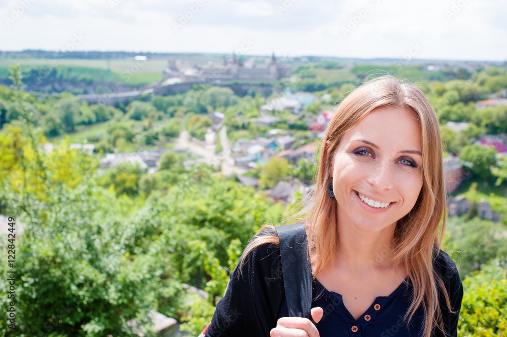 Backpacker. Pretty smiling young woman traveler looking at camera over green landscape background.