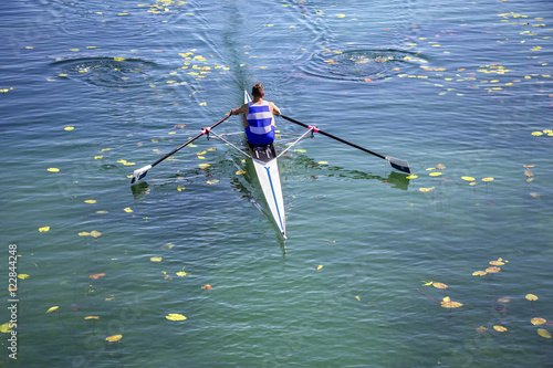A Young single scull rowing competitor paddles on the tranquil