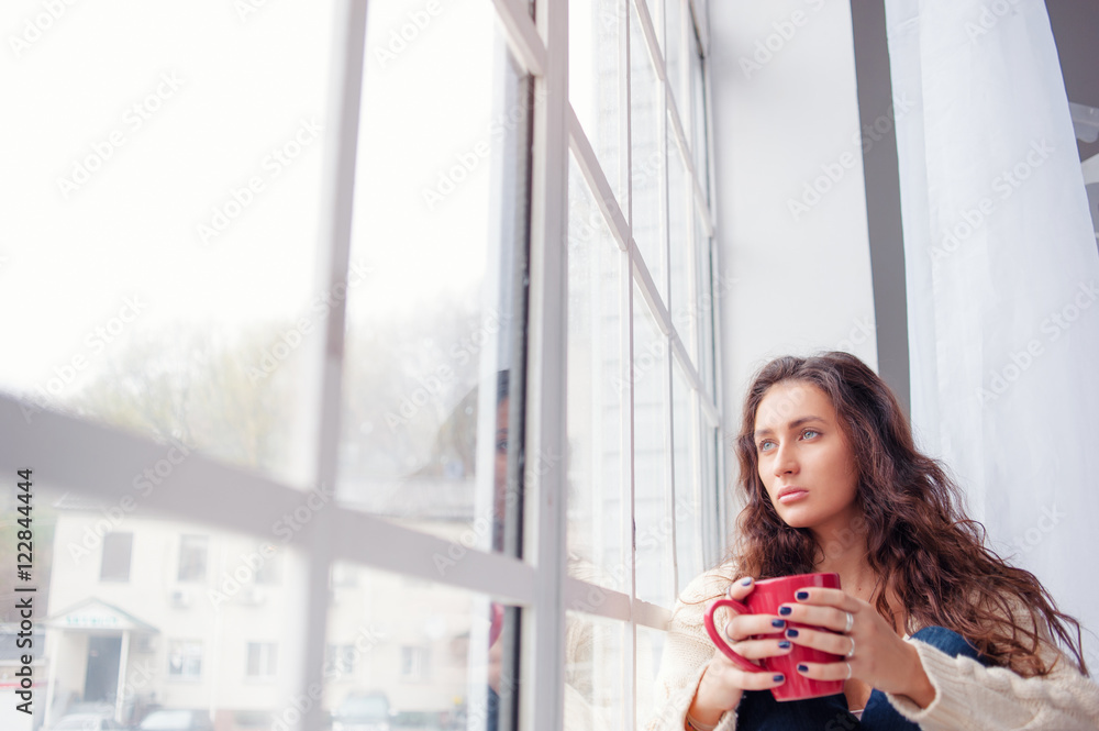 Calm and coziness. Beautiful young woman with cup of tea sitting near the window at home. Calm and coziness. Beautiful young woman with cup of tea sitting near the window at home.