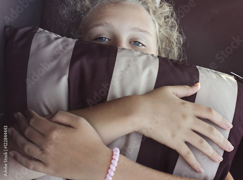 Girl is hiding her face by striped pillow photo