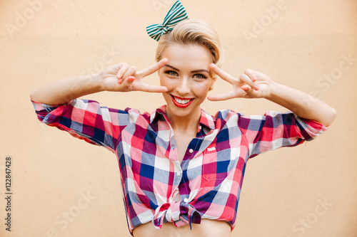 Smiling charming young pin-up woman showing peace sign