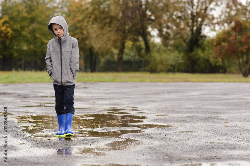 Boy in rubber blue rain boots walking in the rain