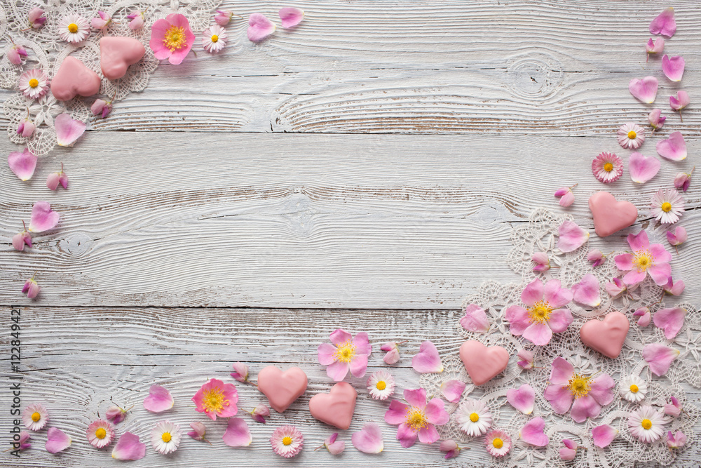 Light wood background with pink flowers, petals, candy in the shape of heart and lace Light wood background with pink flowers, petals, candy in the shape of heart and lace