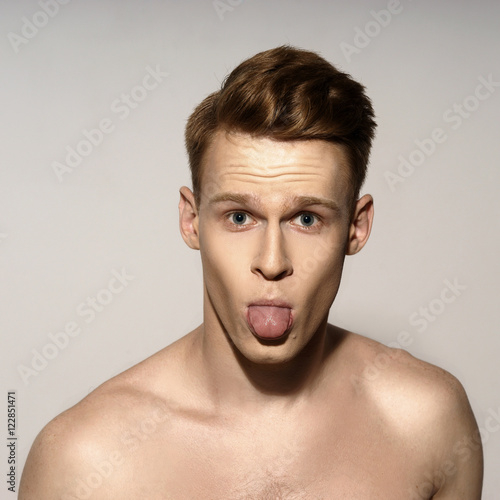 Studio fashion style closeup face portrait of young emotional man looking in camera and showing tongue