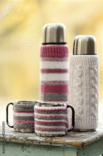 Rustic style. On the old stool is a thermos with cups in knitted