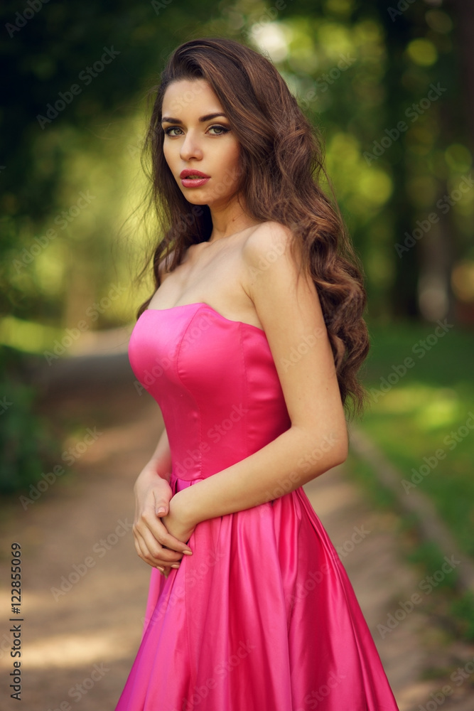 Beauty romantic girl outdoor. Pretty young model dressed in long evening dress posing outdoors at path in the park. Full body Portrait with beautiful bokeh