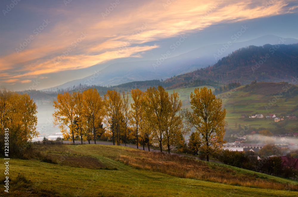 Naklejka premium Mountain road with trees along a path with a mountain village.