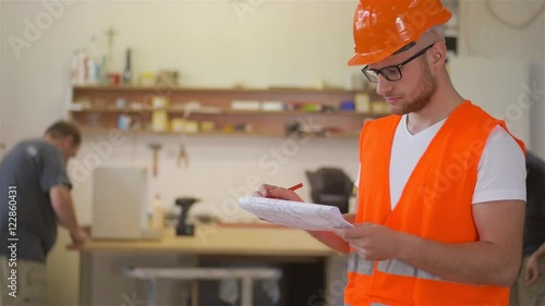 Carpenters is analyzing construction plans using documents and smiling to the camera.