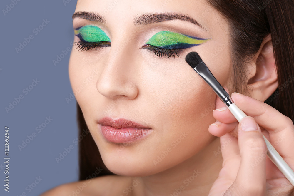 Makeup artist applying makeup on model eyes, on grey background