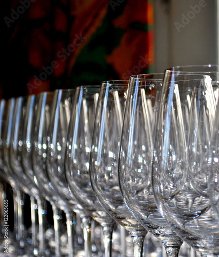 a row of identical empty wine glasses in a daylight with a rich dark green curtain with red-orange pattern in the background photo