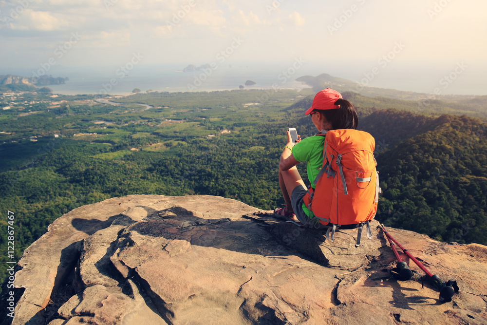 hiker taking photo with smartphone at seaside mountain cliff
