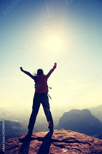 silhouette of free cheering woman hiker open arms at mountain peak